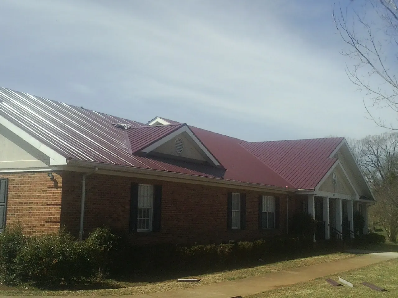 Red metal roof with gabled entries on a long brick building, from a Hail Damage Roof Repair job in Taunton