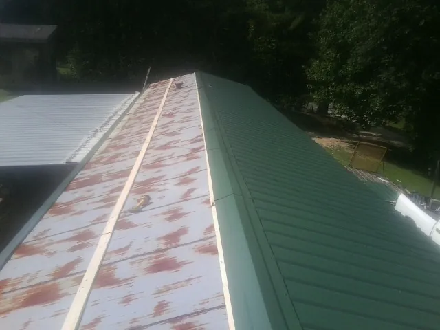Old rusted panels beside newly installed green metal roofing — Wind Damage Roof Repair by Roofing Brothers in Taunton