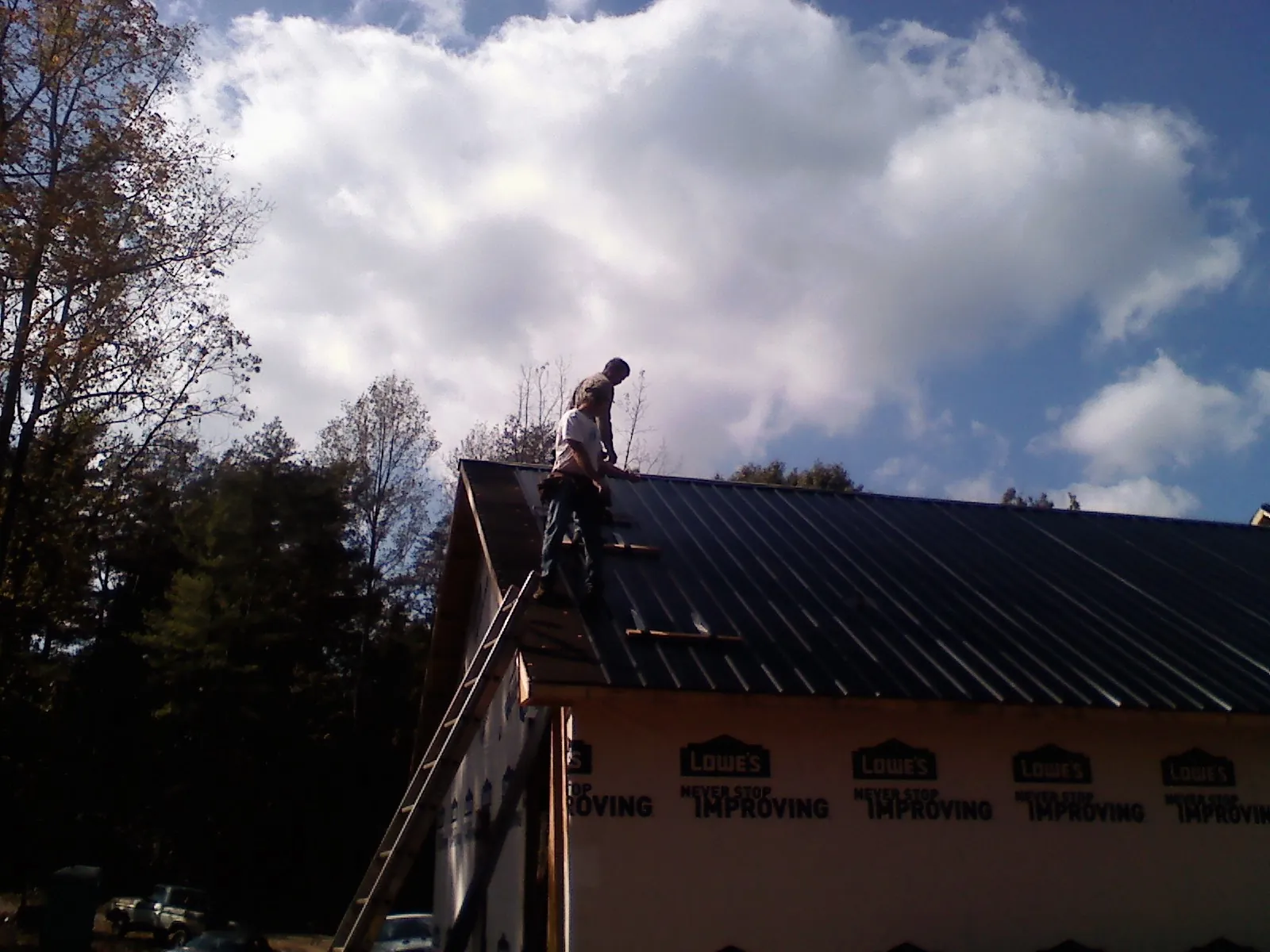 Roofer fastening dark metal panels high against a cloudy sky, from a Roof Inspection job in Taunton