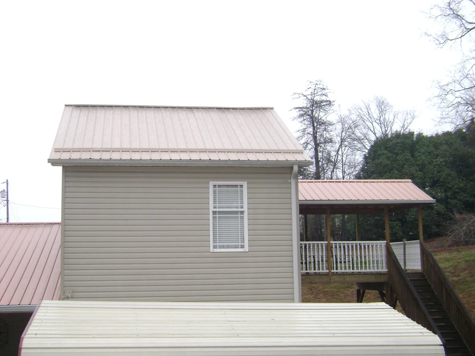 Tan metal roofs on a two story addition and attached porch, from a Roof Replacement job in Taunton